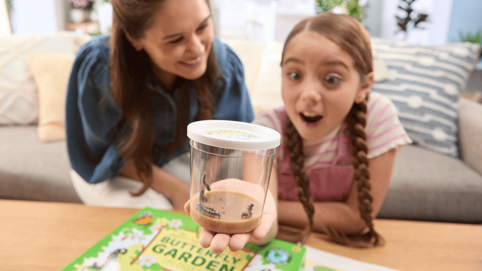 Mother smiling at young daughter with pigtails who smiles in amazement at her Insect Lore Butterfly Garden caterpillars.