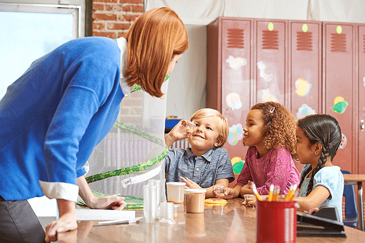 Teacher and students in classroom, watching caterpillars in individual vials, green, pop-up habitat in background.