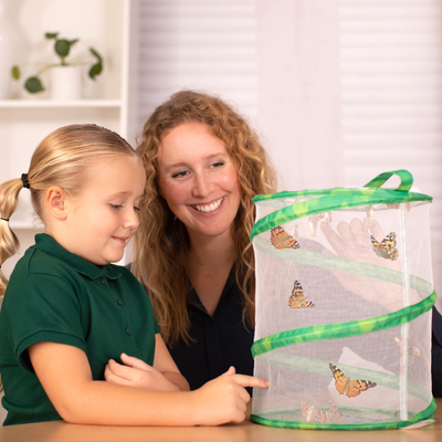 Photo of mom and daughter looking into a Butterfly Garden butterfly habitat with orange and black Painted Lady butterflies