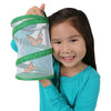Smiling girl holding up Insect Lore Pop-Up Port-A-Bug. Two orange and black butterflies are fluttering in the small, 8 inch tall, green, pop-up, mesh habitat.