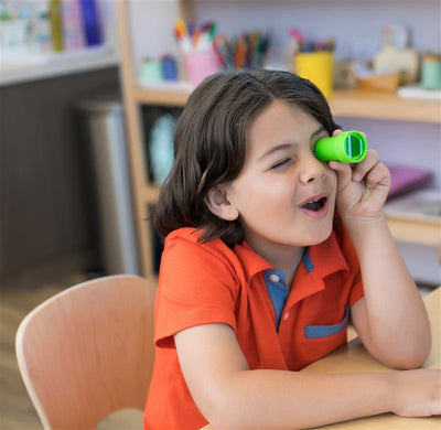 Small boy in orange shirt looking through a green bug eye surprise prism viewer