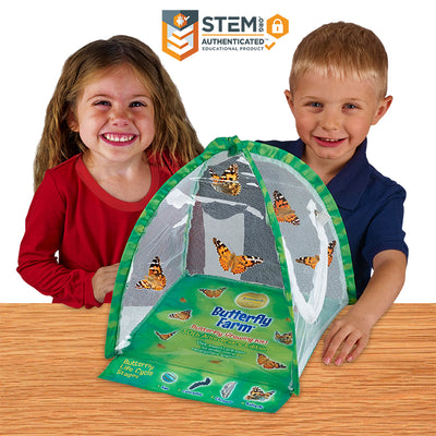 2 happy children with the butterfly farm tent shaped habitat with clear viewing panels and butterflies fluttering inside.