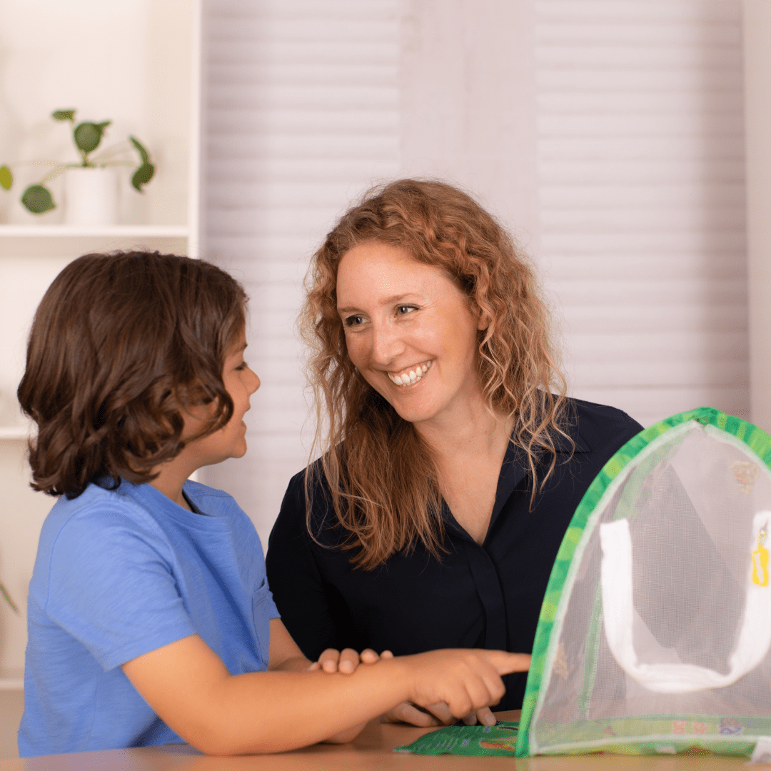 An adult with a child smiling at each other happily with a dome shaped habitat in the foreground